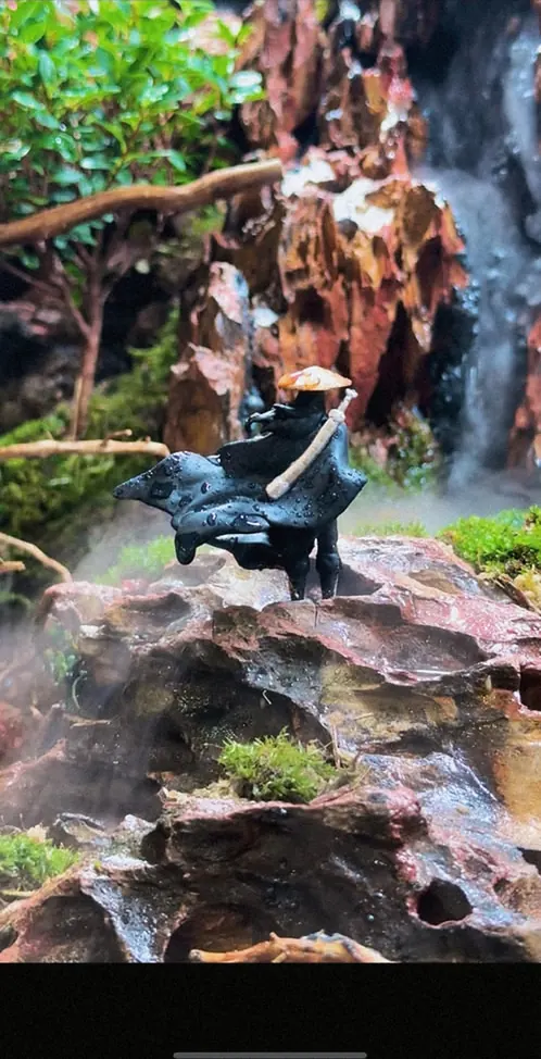 A small figure under the plants of a tall paludarium